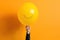 Person holding a balloon. Unrecognizable person holding yellow balloon against orange.