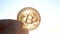 Person holding bitcoin BTC coin in hand on background of shining sun in the sky