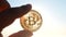Person holding bitcoin BTC coin in hand on background of shining sun in the sky
