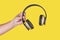 Person holding a brown wireless headphone in a yellow background