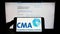 Person holding cellphone with logo of British Competition and Markets Authority (CMA) on screen in front of webpage.