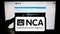 Person holding cellphone with logo of British National Crime Agency (NCA) on screen in front of webpage.