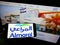 Person holding cellphone with logo of Saudi Arabian dairy company Almarai Company on screen in front of business webpage.
