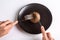A person is holding a cutlery fork and knife and cutting a raw one jersey cow mushroom on a black plate on a white