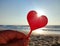 Person holding in fingers hand stick in shape red heart on background sea