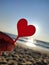Person holding in fingers hand stick in shape red heart on background sea