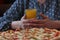 Person holding a glass of orange juice and pizza