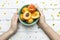 A person holding a green bowl of peaches with yellow flowers spread on a wooden surface