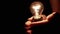 Person Holding in Hands a Luminous Included Edison Light Bulb in a Dark Room