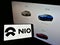 Person holding mobile phone with business logo of Chinese electric car manufacturer NIO Inc. on screen in front of web page.