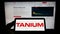 Person holding mobile phone with logo of American cybersecurity company Tanium Inc. on screen in front of web page.