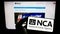 Person holding mobile phone with logo of British National Crime Agency (NCA) on screen in front of web page.