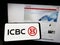 Person holding mobile phone with logo of Chinese financial services company ICBC on screen in front of business web page.