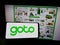 Person holding mobile phone with logo of Indonesian company GoTo Group on screen in front of business web page.
