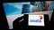 Person holding mobile phone with logo of Malaysian carrier Axiata Group Berhad on screen in front of business web page.