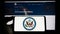 Person holding mobile phone with seal of United States Department of State (DOS) on screen in front of web page.