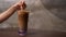 A person holding the paper straw and stirring the ice coffee.