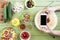 Person holding smartphone with blank screen and photographing spaghetti and fresh vegetables on wooden table