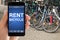 Person Holding Smartphone In Front Of Public Bike Rental Station