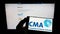 Person holding smartphone with logo of British Competition and Markets Authority (CMA) on screen in front of website.