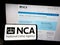 Person holding smartphone with logo of British National Crime Agency (NCA) on screen in front of website.