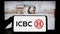 Person holding smartphone with logo of Chinese financial services company ICBC on screen in front of website.