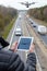 Person holding tablet with drone image as a real drone flies above the road.