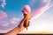 a person holding up a pink ice cream cone in the sunny sky, in the style of lush colors, eye-catching composition