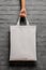 A person holding a white shopping bag against a brick wall. Generative AI image. Blank tote bag mockup.