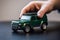 A person holds in hand a scaled model of green SUV car . Concept of buying a dream car. Generative ai