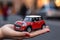 A person holds in hand a scaled model of red hatchback car. Concept of buying a dream car. Generative ai