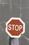 Person holds up big stop road sign. Bold red against cracked gray wall.