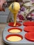 Person at home filling red pastry molds to cook cup cakes