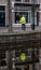 Person and its reflection of a person in a yellow jacket in the water of a canal in front of a shop window