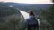 Person looking down at beautiful river valley from high point of mountains, back view, middle shot, handheld