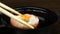 Person lowers his sushi in soy sauce by chopsticks. Close up