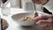 Person mixes tasty fresh cereals in plate at table in room