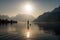 person, paddleboarding in quiet lake, with mountains and sun visible in the background