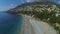 Person paragliding over seashore past buildings and hills, getting ready to land