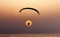 Person parasailing in the crystal clear waters of a tropical beach as the sun sets in the distance.