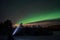 Person pointing flashlight beam towards aurora borealis on winter night sky