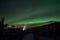 Person pointing flashlight beam towards aurora borealis on winter night sky in spruce tree field