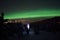 Person pointing flashlight beam towards aurora borealis on winter night sky in spruce tree field
