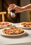 Person pouring oily sauce on a delicious freshly-baked pizza on a plate