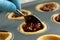 Person putting mince pie filling onto pastry base in a metal baking tray