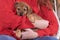 Person in a red knitted sweater hugs a brown puppy