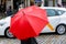 Person with red rain umbrella crosses a city street