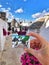 Person's hand holding a travel card in front of the iconic Alberobello, Italy