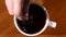 Person`s hand stir sugar in cup of black coffee