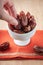 A person`s hand taking a dried organic date from a bowl on a brightly colored orange cloth.